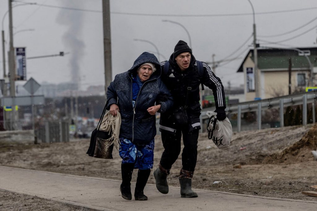 Мужчина помогает бабушке убежать в укрытие от обстрела российскими войсками в Ирпене, рядом с городом Буча