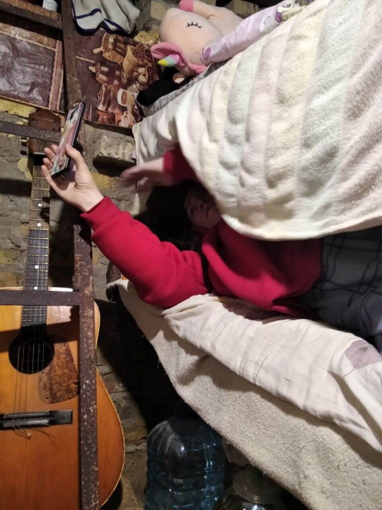 Ребенок лежит с телефоном на кровате в подвале Титовых, также рядом с городом Буча