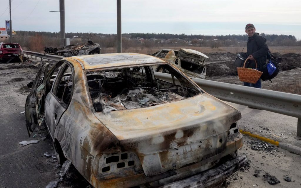 Житель Ирпеня, убегая из города, идет мимо сгоревшей машины по дороге в Киев, недалеко от города Буча