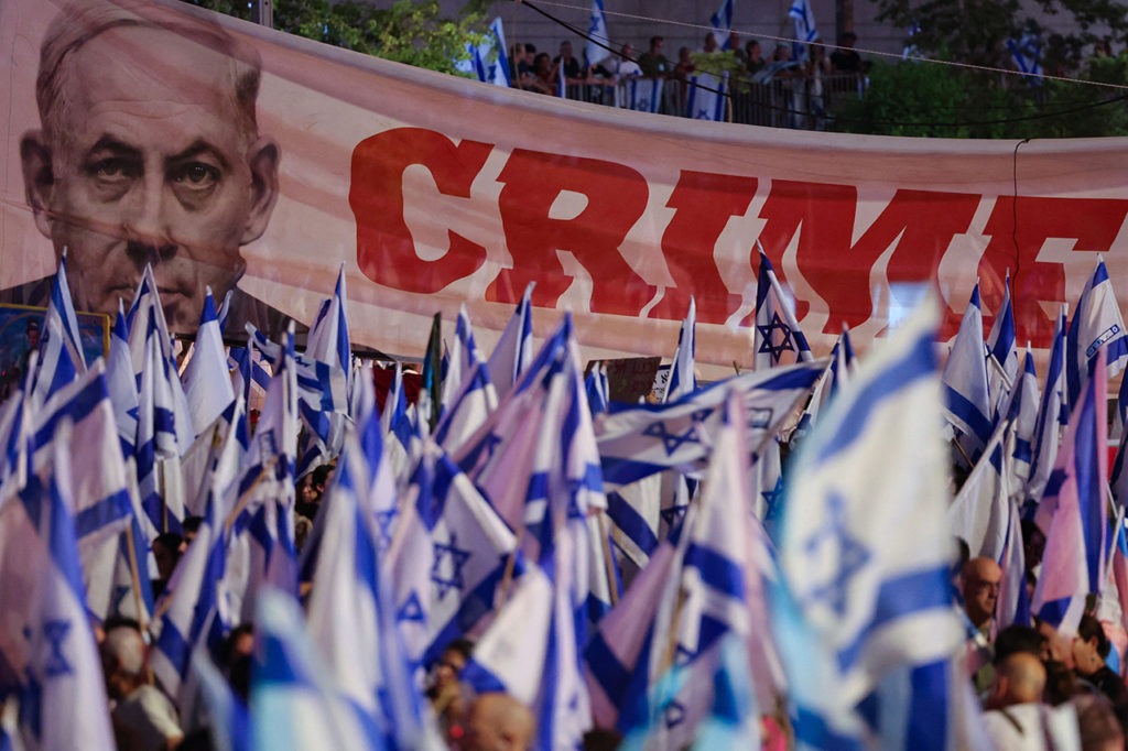 Протестующие размахивают национальными флагами и транспарантом с изображением премьер-министра Биньямна Нетаньяху во время марша против плана реорганизации судебной системы Израиля в Тель-Авиве.