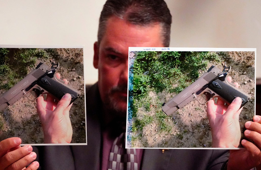 Следователь держит фотографии пистолетов, которые хранились в ноутбуке одного из членов семьи Вагнер.