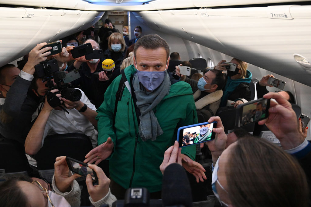 Пока политик находился на лечении в Германии, ФСИН обвинила его в нарушении условий условного срока, и теперь ему грозило реальное лишение свободы. Несмотря на пережитое отравление и угрозу тюрьмы, 17 января 2021 года Алексей Навальный прилетел в Россию. На фото Навальный пробирается к своему месту перед взлетом в Москву