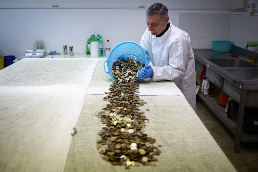 Волонтер католической организации Caritas Энрико Кьолини высыпает монеты и готовится сушить их на специальном столе. 26 февраля 2024 года