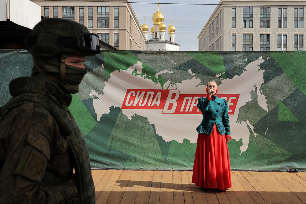 Военный на фоне женщины, которая поет на фоне баннера «Сила в правде»